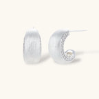 Close-up of small silver-plated hoop earrings with brushed texture and a row of sparkling zircon crystals on white background
