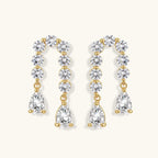Gold-plated earrings with vertical line of clear crystals and teardrop pendants on neutral background