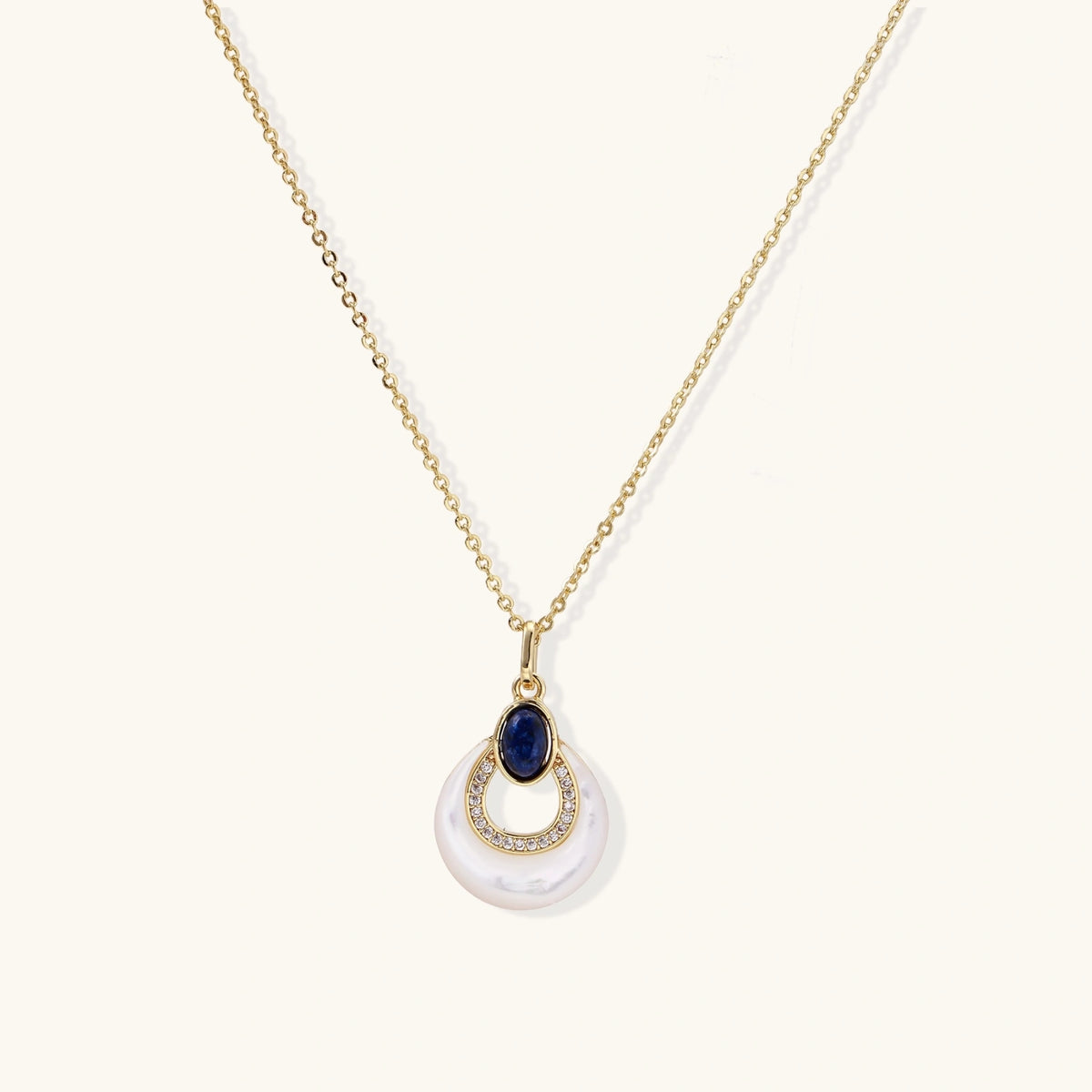 Gold plated chain necklace with a white MOP crescent pendant, blue lapis lazuli oval and sparkling stone accents on a cream background.