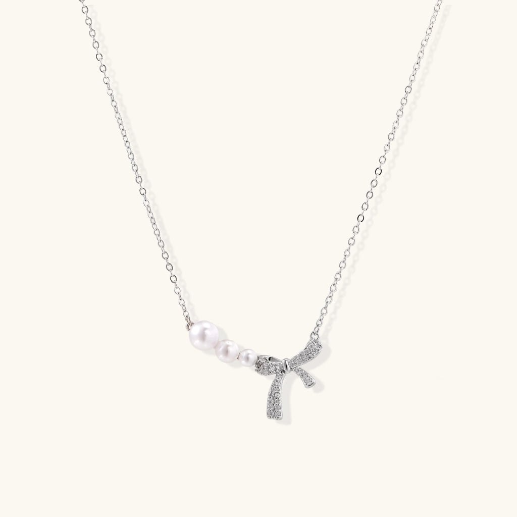 Delicate white gold plated necklace with freshwater pearls and sparkly crystal bow pendant on white background