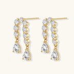 Gold-plated earrings with vertical line of clear crystals and teardrop pendants on neutral background